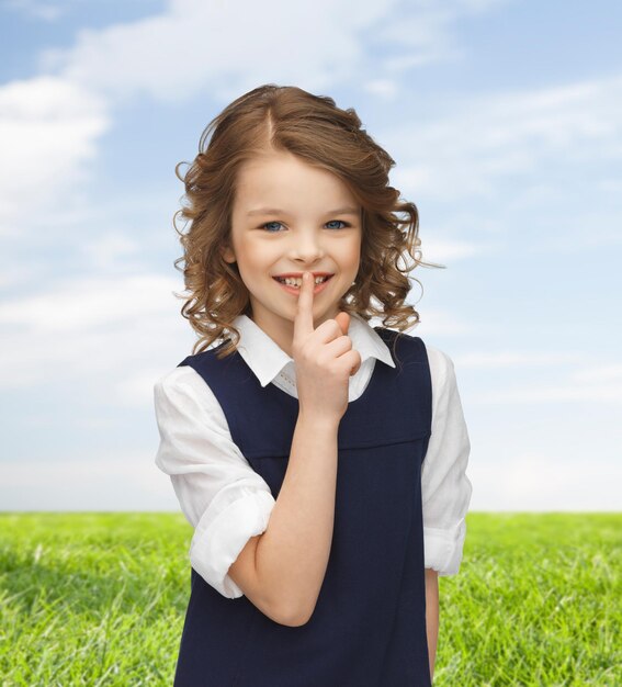 Mensen, kinderen, geheimhouding en mysterieconcept - gelukkig meisje dat een stil gebaar toont over blauwe lucht en grasachtergrond