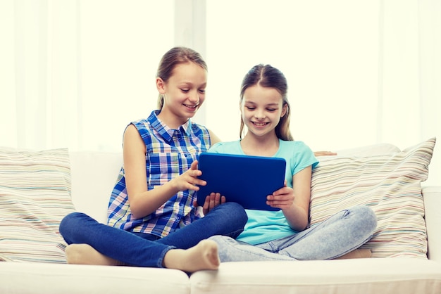 mensen, kinderen, technologie, vrienden en vriendschapsconcept - gelukkige kleine meisjes met tablet pc-computer die thuis op de bank zit