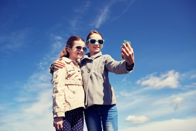 mensen, kinderen, technologie, vrienden en vriendschapsconcept - gelukkige meisjes met smartphone die selfie buitenshuis nemen
