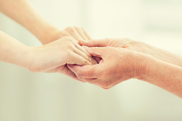 mensen, leeftijd, familie, zorg en ondersteuning concept - close-up van senior vrouw en jonge vrouw hand in hand