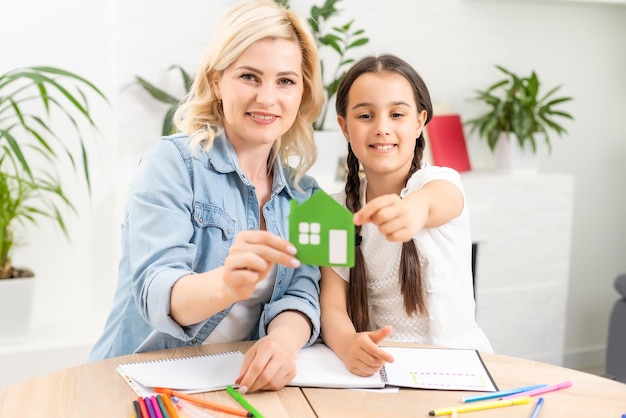 mensen, liefdadigheid, familie en thuisconcept - close-up van vrouw en meisje die groenboekhuisknipsel in holle handen houden.