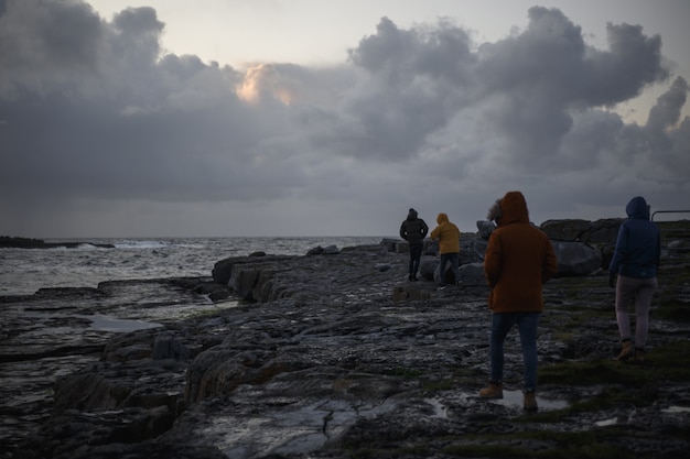 Foto mensen lopen op een donker zeegezicht met rotsen en wolken