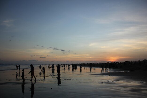 Mensen lopen op het strand bij zonsondergang met de ondergaande zon achter hen.