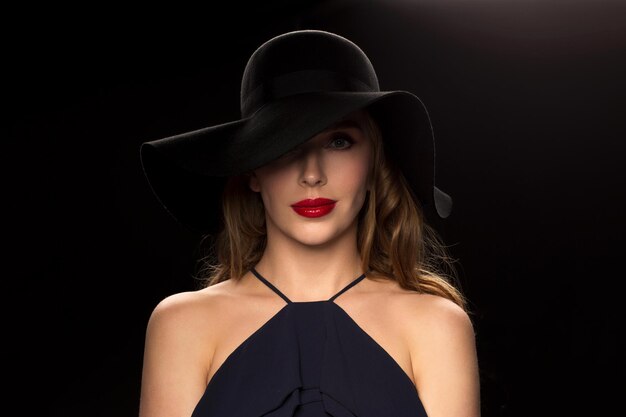 mensen, luxe en modeconcept - mooie vrouw in zwarte hoed op donkere achtergrond