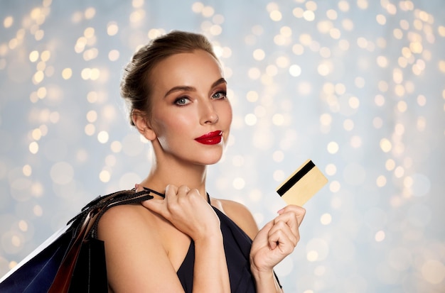 mensen, luxe en verkoopconcept - mooie vrouw met creditcard en boodschappentassen over de achtergrond van vakantieverlichting