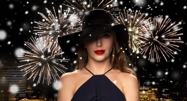 mensen, luxe, kerstmis, nieuwjaar en wintervakantie concept - mooie vrouw in zwarte hoed 's nachts singapore stad en vuurwerk achtergrond met sneeuw