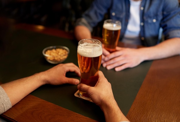 mensen, mannen, vrije tijd, vriendschap en communicatieconcept - close-up van mannelijke vrienden die tapbier drinken in bar of pub