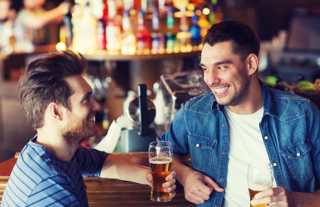 mensen, mannen, vrije tijd, vriendschap en communicatieconcept - gelukkige mannelijke vrienden die bier drinken en praten in de bar of pub