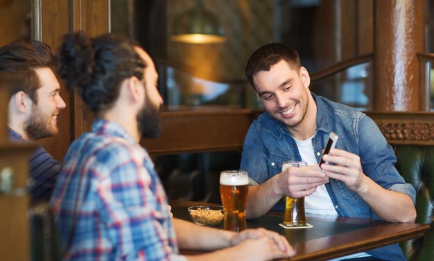 mensen, mannen, vrije tijd, vriendschap en technologieconcept - gelukkige mannelijke vrienden met smartphone die bier drinken bij bar of pub