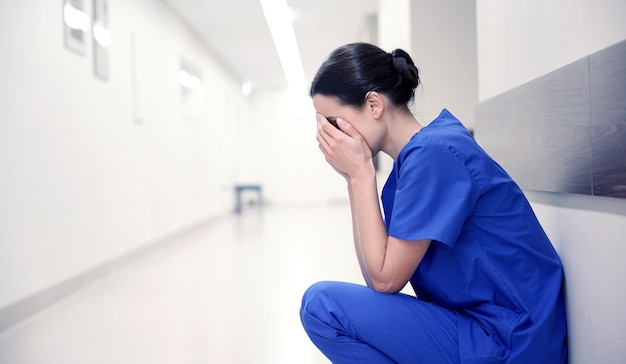 mensen, medicijnen, gezondheidszorg en verdriet concept - verdrietig of huilende vrouwelijke verpleegster in de ziekenhuisgang