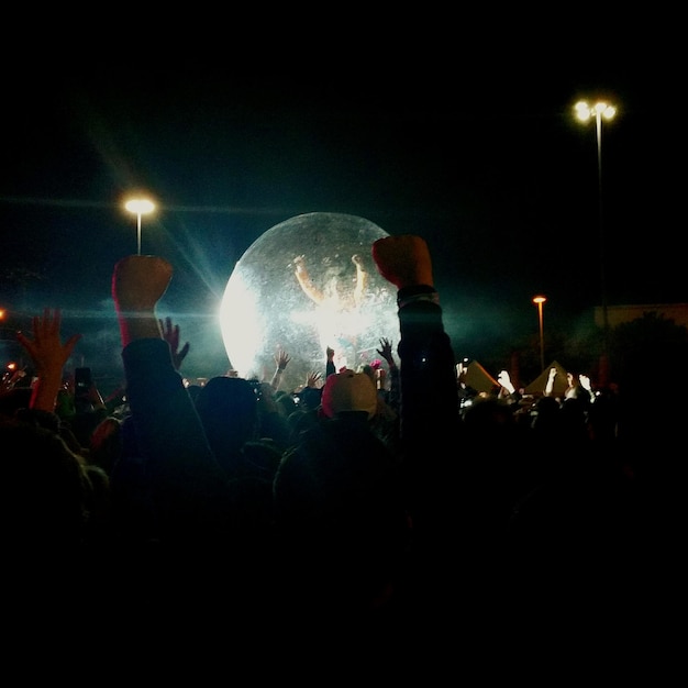 Foto mensen met hun armen omhoog tegen zorb bal in concert tegen de hemel's nachts