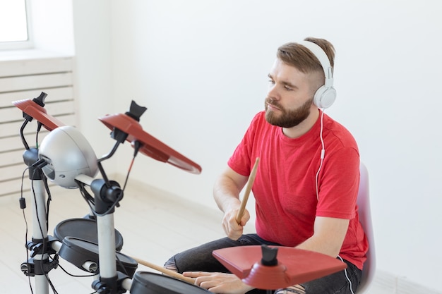 Mensen, muziek en hobby concept - Man met witte koptelefoon die de drums speelt op een lichte achtergrond.