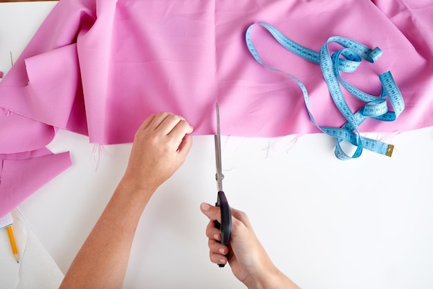 mensen, naaien, handwerken, naaien en maatwerk concept - vrouw met kleermakersschaar of -schaar die stof uitknipt in de studio