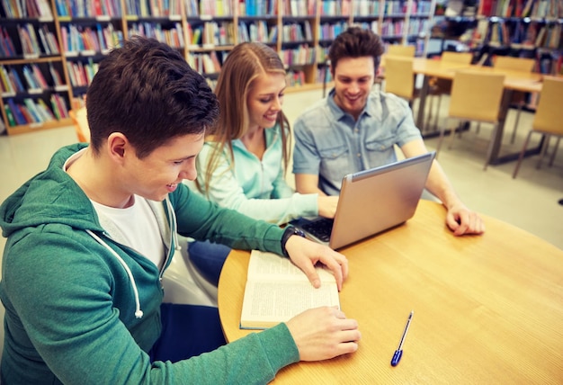 mensen, onderwijs, technologie en schoolconcept - gelukkige studenten met laptopcomputer en boeken in bibliotheek