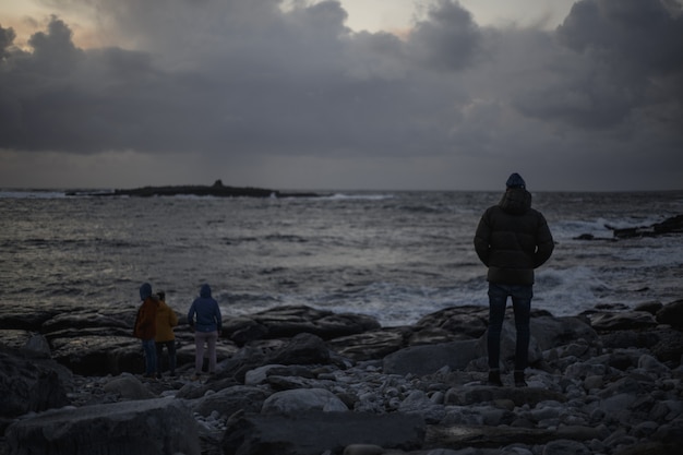 Foto mensen op een donker zeegezicht met rotsen en wolken