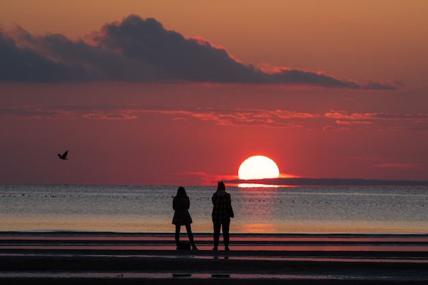 Mensen op het strand genieten van een prachtige zonsondergang in het herfstseizoen, kijken naar de ondergaande zon in de zee en de kleurrijke lucht