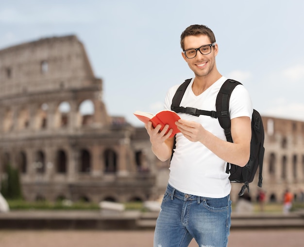 Foto mensen, reizen, toerisme en onderwijsconcept - gelukkige jonge man met rugzak en boek die over de achtergrond van het colosseum reizen