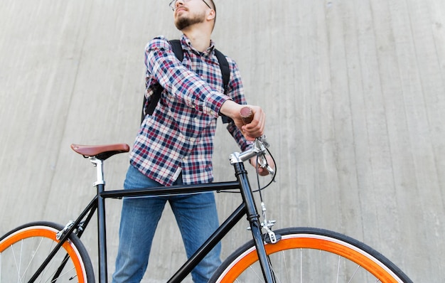 mensen, reizen, toerisme, vrije tijd en levensstijl - close-up van jonge hipster man met fiets met vaste versnelling en rugzak op straat in de stad