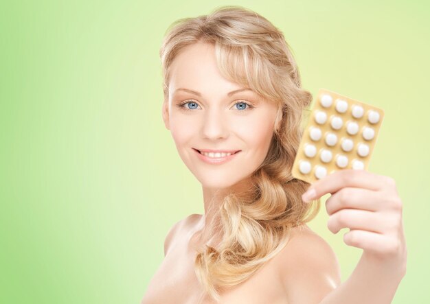 mensen, schoonheid, gezondheidszorg en geneeskundeconcept - gelukkige jonge vrouw die pakket pillen over groene achtergrond houdt