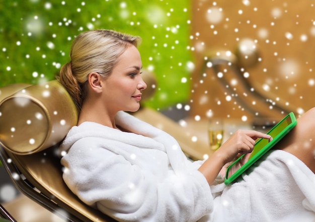 mensen, schoonheid, levensstijl, technologie en ontspanning concept - mooie jonge vrouw in witte badjas met tablet pc computer sociale netwerken in spa met sneeuweffect