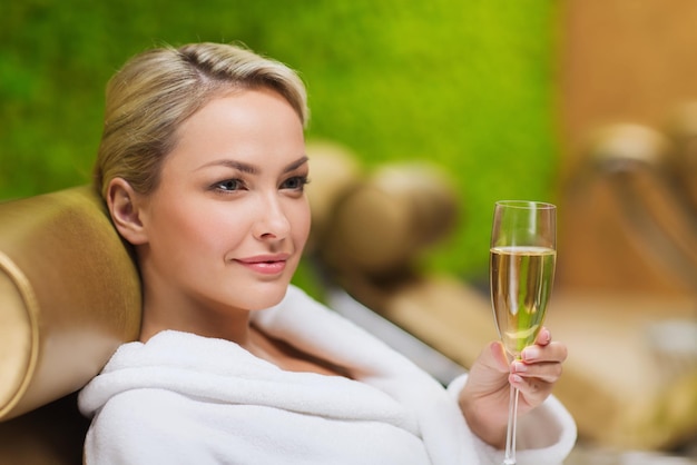 Mensen, schoonheid, levensstijl, vakantie en ontspanning concept - mooie jonge vrouw in witte badjas liggend op chaise-longue en champagne drinken in de spa