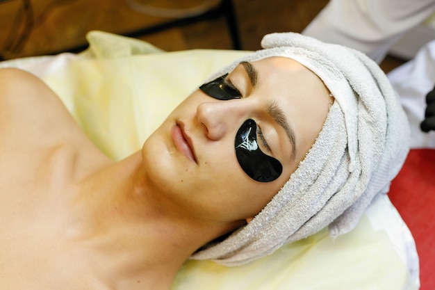 Mensen, schoonheid, spa, cosmetologie en technologie concept - Spa salon. De schoonheidsspecialist zet een masker op het gezicht van een jonge man.