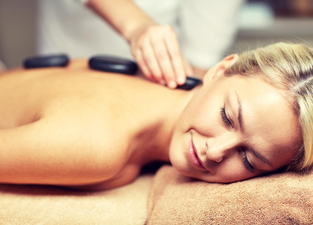 Foto mensen, schoonheid, spa, gezonde levensstijl en ontspanningsconcept - close-up van mooie jonge vrouw met hotstone-massage in spa