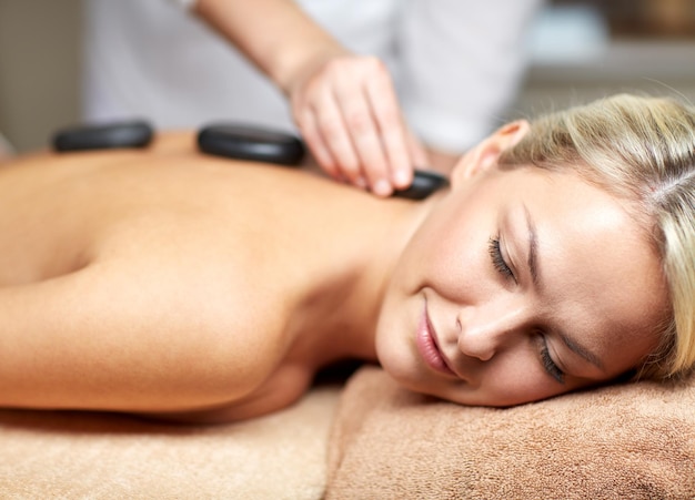 mensen, schoonheid, spa, gezonde levensstijl en ontspanningsconcept - close-up van mooie jonge vrouw met hotstone-massage in spa