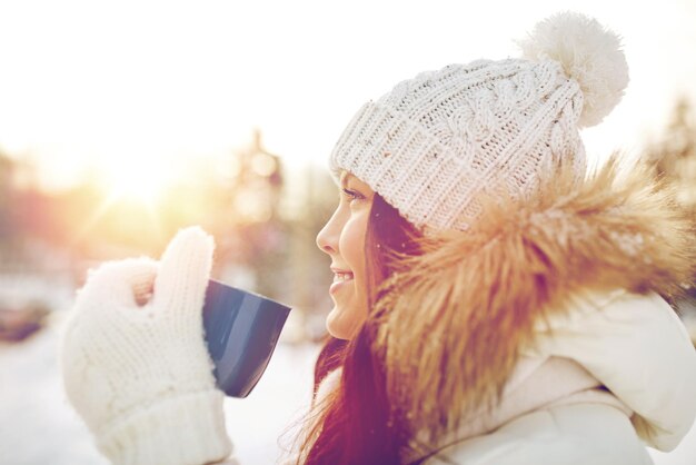 Foto mensen, seizoen, drankjes en vrije tijd concept - gelukkige jonge vrouw met kopje thee buiten in de winter