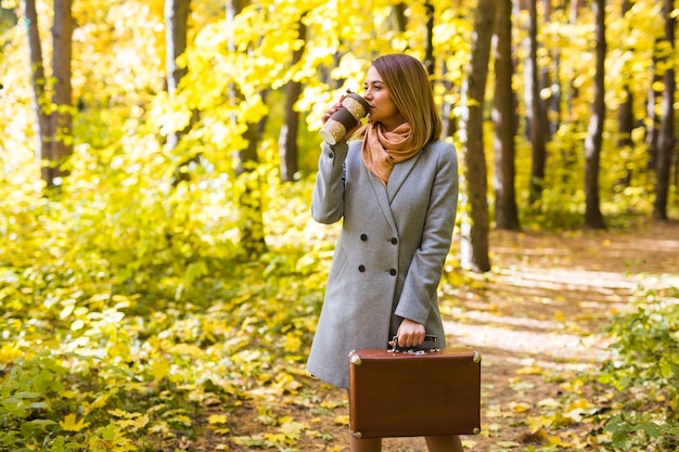 Mensen, seizoen en mode concept - jonge vrouw koffie drinken in herfst park