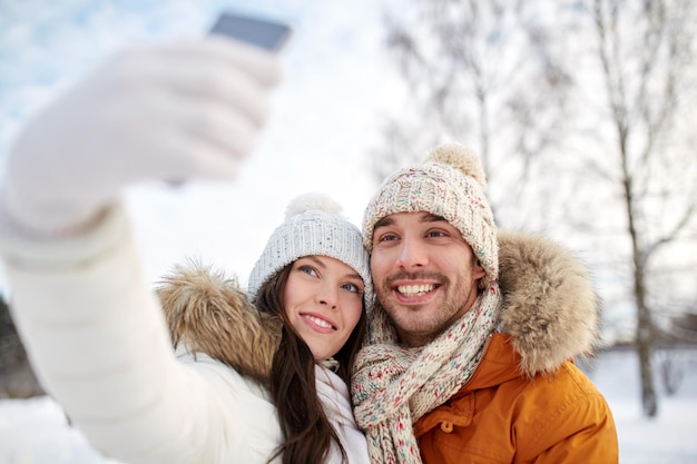Mensen, seizoen, liefde, technologie en vrije tijdsconcept - gelukkig paar dat selfie door smartphone over winterachtergrond neemt