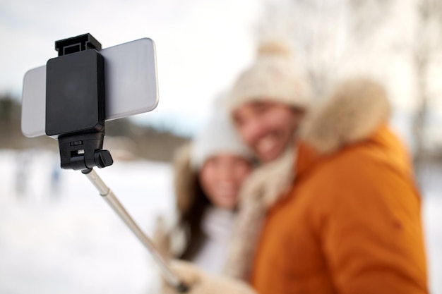 mensen, seizoen, technologie en winterconcept - gelukkig stel dat foto's maakt met smartphone selfie stick buitenshuis