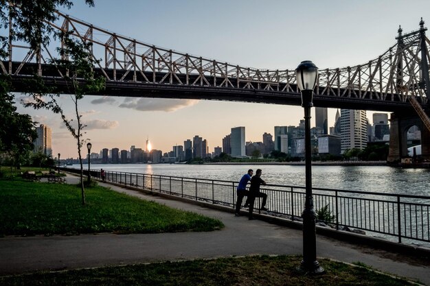 Foto mensen staan bij de reling tegen de rivier met de stad tijdens de zonsondergang