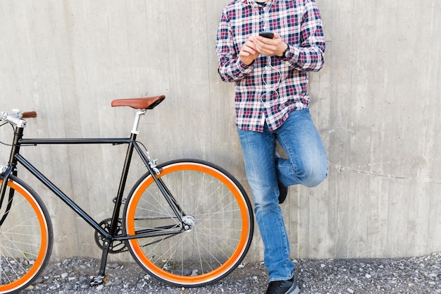 mensen, stijl, technologie, vrije tijd en levensstijl - close-up van jonge hipster man in oortelefoons met smartphone en fiets met vaste versnelling luisterend naar muziek op straat in de stad