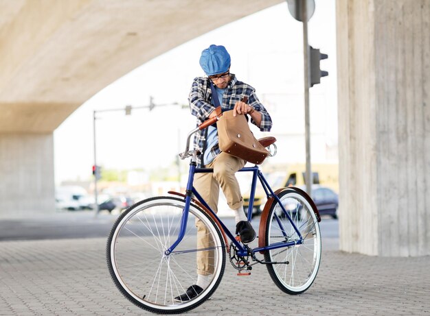 Foto mensen, stijl, vrije tijd en levensstijl - hipster man op zoek naar iets in zijn schoudertas met vaste versnellingen op straat in de stad