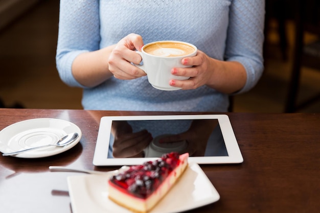 mensen, technologie en lifestyle concept - close-up van handen met koffiekopje, tablet pc-computer en bessencake op tafel