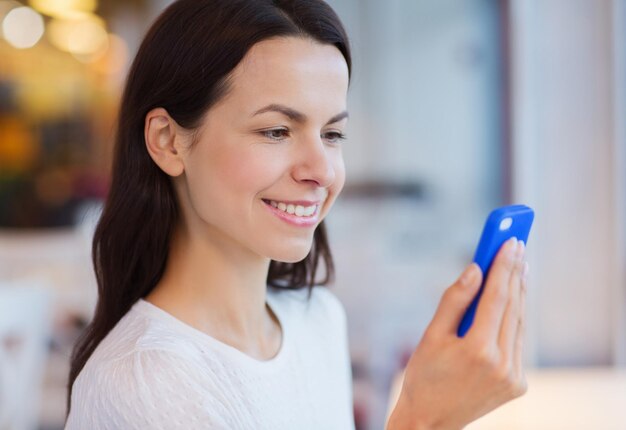 mensen, technologie en lifestyle concept - close-up van lachende jonge vrouw die bericht leest van smartphone in café