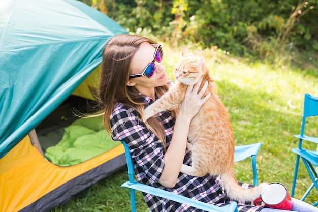 Mensen, toerisme en natuurconcept - Vrouw in zonnebril die een kat aait die dichtbij de tent zit.