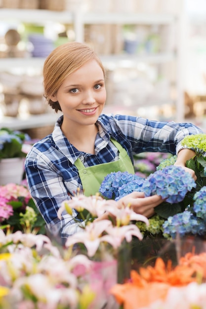 Mensen, tuinieren en beroep concept - gelukkige vrouw of tuinman die voor bloemen in de kas zorgt