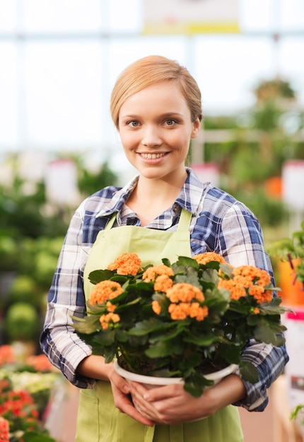 mensen, tuinieren en beroep concept - gelukkige vrouw of tuinman met bloemen in kas