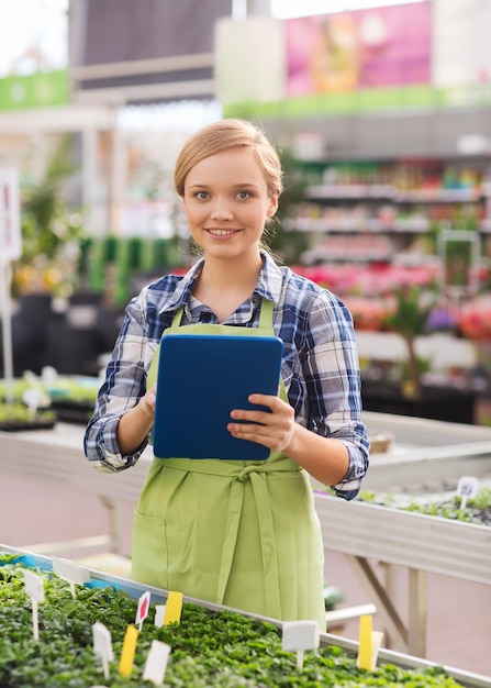 Foto mensen, tuinieren, technologie en beroep concept - gelukkige vrouw of tuinman met tablet pc-computer en zaailing in kas