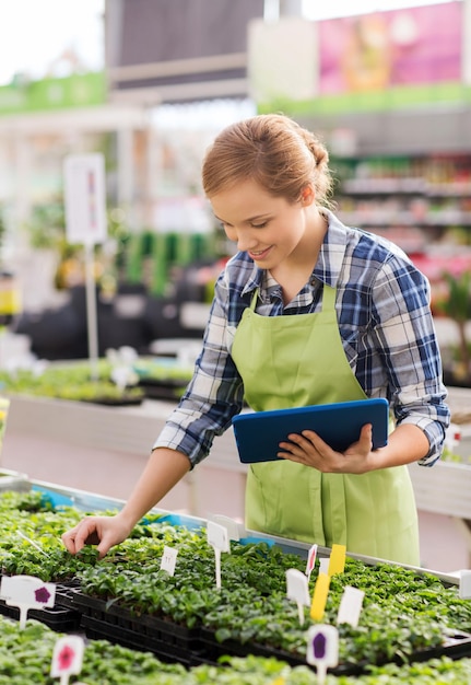 mensen, tuinieren, technologie en beroep concept - gelukkige vrouw of tuinman met tablet pc-computer en zaailing in kas