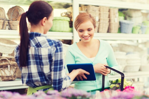 mensen, tuinieren, winkelen, verkoop en consumentisme concept - gelukkige tuinman met tablet pc die vrouw helpt met het kiezen van bloemen bij bloemenwinkel