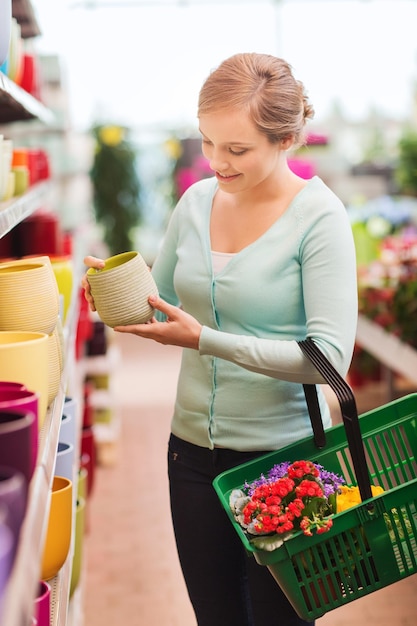 Mensen, tuinieren, winkelen, verkoop en consumentisme concept - gelukkige vrouw met mand bloemen kopen en bloempot kiezen bij bloemenwinkel