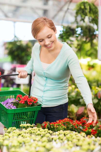 mensen, tuinieren, winkelen, verkoop en consumentisme concept - gelukkige vrouw met mand die bloemen in kas kiest en koopt