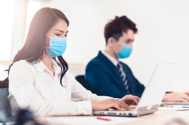 Mensen uit het bedrijfsleven die een medisch gezichtsmasker dragen terwijl ze op kantoor werken