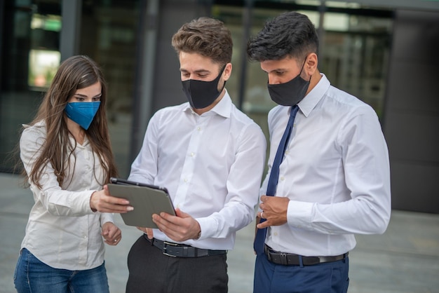 Mensen uit het bedrijfsleven die een tablet buiten gebruiken met een beschermend masker tegen covid 19