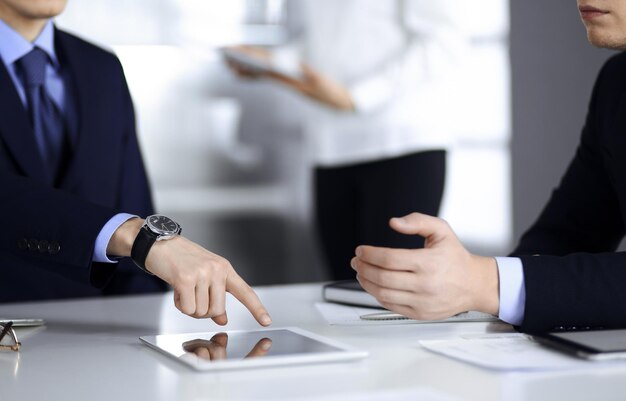 Mensen uit het bedrijfsleven gebruiken een tabletcomputer voor de bespreking van hun nieuwe project, staande in een modern kantoor. onbekende zakenman of mannelijke ondernemer met een collega op de werkplek. teamwerk en partnerschap