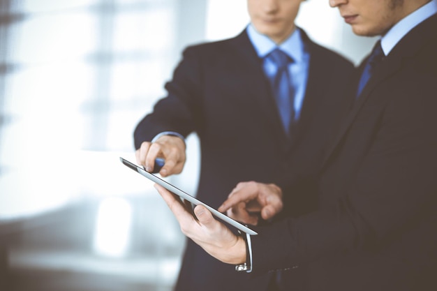 Mensen uit het bedrijfsleven gebruiken een tabletcomputer voor de bespreking van hun nieuwe project, staande in een modern kantoor. Onbekende zakenman of mannelijke ondernemer met een collega op de werkplek. Teamwerk en partnerschap