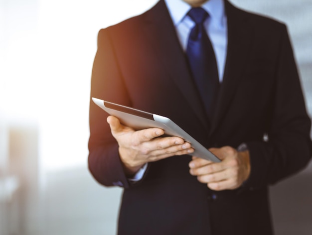 Mensen uit het bedrijfsleven gebruiken een tabletcomputer voor de bespreking van hun nieuwe project, staande in een zonnig modern kantoor. Onbekende zakenman of mannelijke ondernemer met een collega op de werkplek.